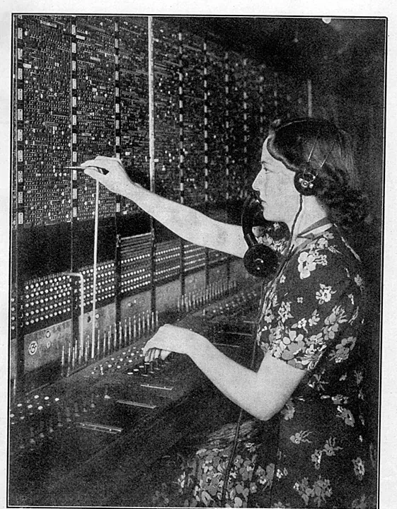 A printed page: a young telephonist in a floral dress and headset sits in profile at a tall switchboard, her right arm raised to put a plug into the field of jacks, her left hand on the keyshelf.