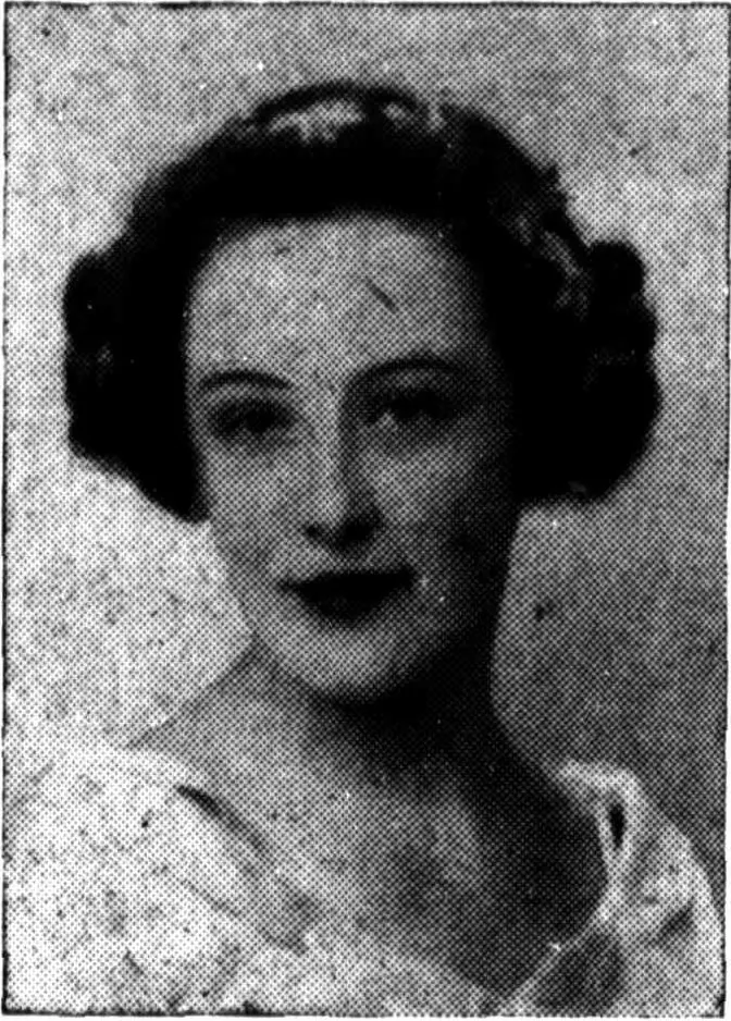 A newspaper studio portrait of a young woman with dark hair set in rolls about her face, dark lipstick and a pale ruffled blouse.